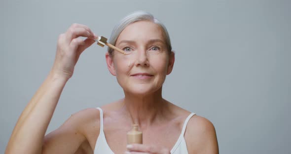 An Older Model Applies Foundation to Her Face and Smearing the Drops