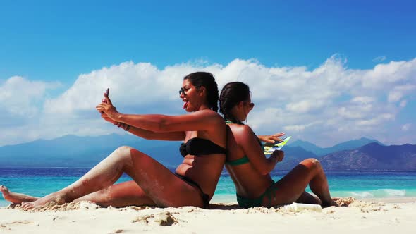 Ladies together best friends on idyllic shore beach holiday by blue green sea and white sand backgro