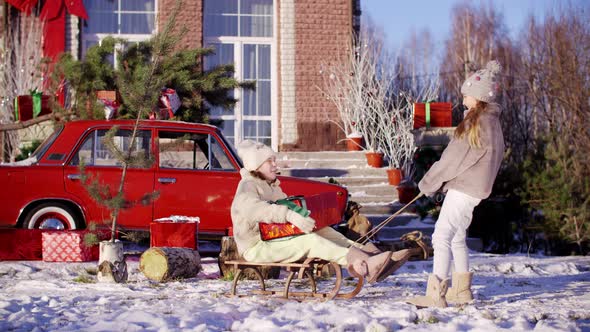 Two Funny Teenage Girls Sledding on Christmas Tree While Holidays. Happy Girlfriends with Christmas