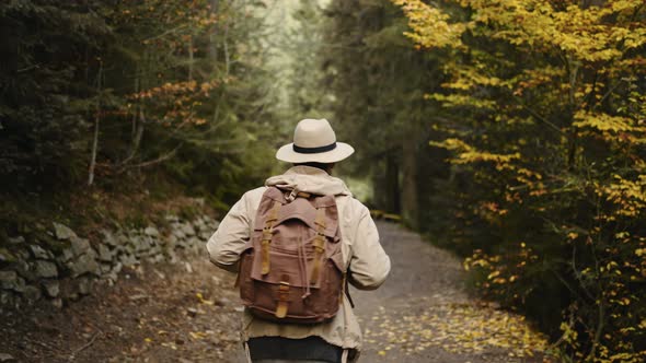 Happy Hipster Man in Casual Wear and Hat Hiking in Forest in Autumn