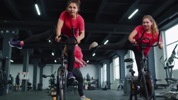 Group Athletic Girls Performing Aerobic Riding Training Exercises on Cycling Stationary Bike in Gym