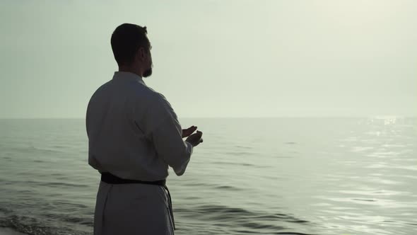 Athletic Man Honing Karate Technique Enjoying Sunset on Beach Back View