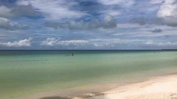 Camera pan along caribbean palm fringed beach with people enjoying the clear water