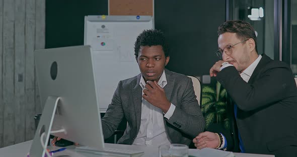 European and African in the Office in Front of the Computer Showing Happy Emotions