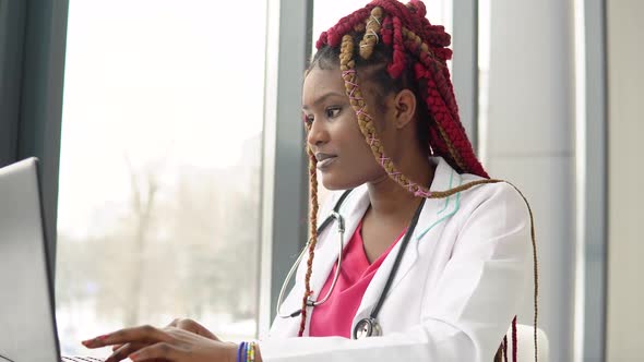 Young African American Female Doctor Working on Laptop in Modern Clinic