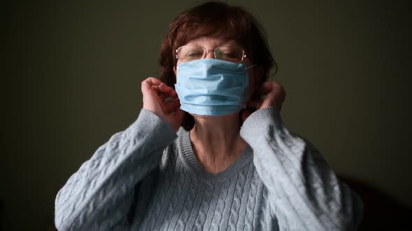 woman puts on a medical mask on a dark background and then removes it