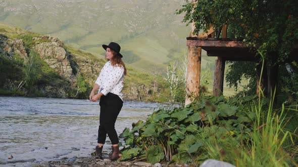 Attractive Brunette in a Hat and a White Shirt in Peas Enjoys Nature in the Mountains. Young Woman