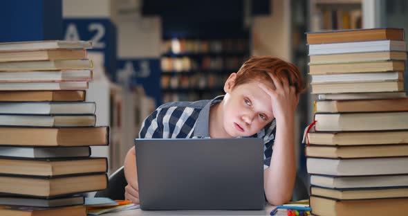 Bored Teen Boy Student Sitting at Table in Campus Open Space Library