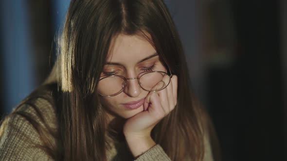 Tired Student Leaned on Hand Corrects Glasses and Thinks in a Library at Night