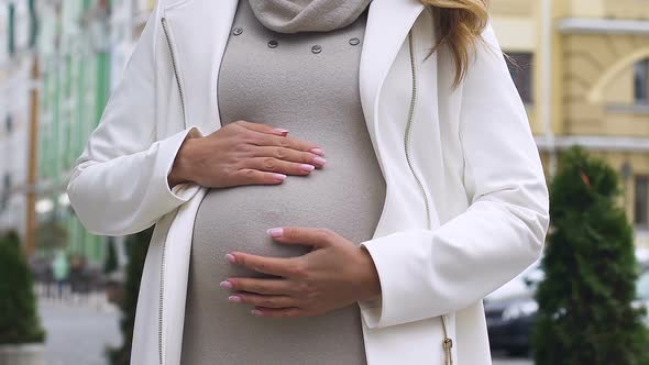 Happy Young Pregnant Lady Stroking Belly and Smiling at Camera Governmental Help