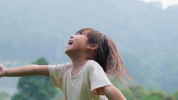 Cute little girl having fun catching rain drops. Kids play in summer rain. Child playing outdoor.