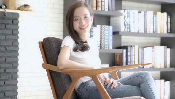 Beautiful portrait young asian woman sitting on chair with smile and happy at living room.