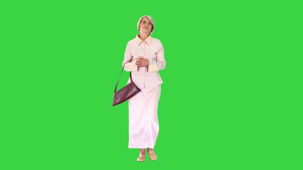Smiling Senior Lady in Glasses and with a Handbag Walking on a Green Screen, Chroma Key.