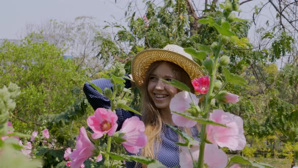 Happy Smiling Travel Woman Resting in Garden with Pink Flowers in Sunny Day