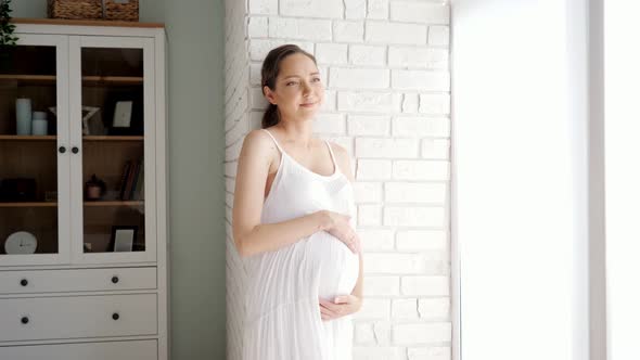 Future Mother Touches Tummy Standing Near Brick Wall in Room