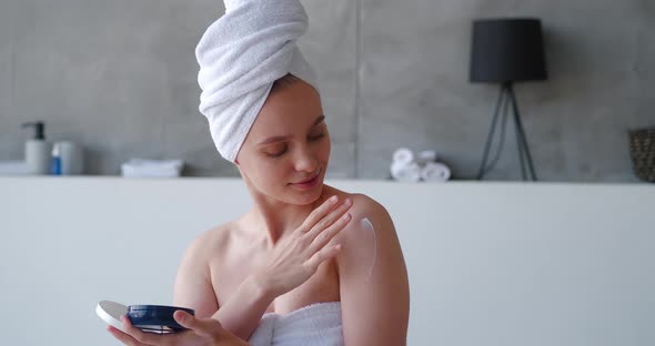 Closeup of a Pretty Woman Wrapped in White Bath Towel in Bathroom Opening a Container with Beauty