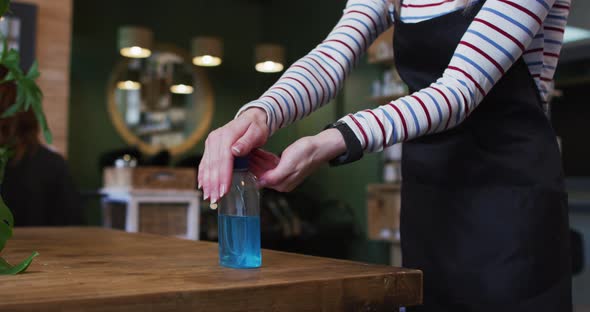 Mid section of female hairdresser sanitizing her hands at hair salon