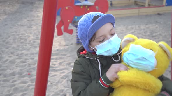 Portrait of Cute Boy in Face Mask Hugging Yellow Teddy Bear and Looking at Camera