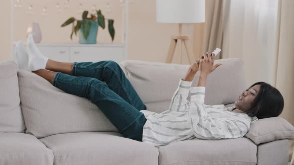 Relaxed Carefree Young Calm Woman Lying on Comfortable Couch in Cozy Living Room Typing Message on