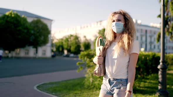 Caucasian Young Pretty Woman Delivery Worker in Medical Mask Walking the Street and Carrying Packet