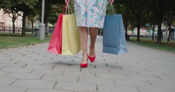 A Woman in Red Highheeled Shoes Carries Multicolored Shopping Bags From a Fashion Store