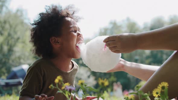 Black Little Girl Eating Cotton Candy From Her Mother's Hands Outdoors