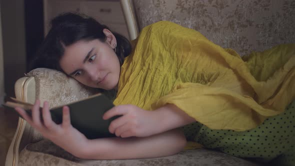Pretty Girl Reading a Book in the Evening Lying on the Couch