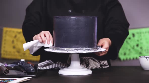 Step by step. Baker frosting multilayer chocolate cake with a black italian buttercream frosting.