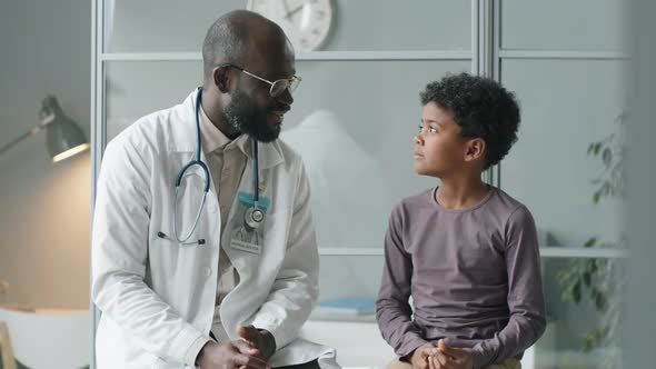 Portrait of Cheerful African American Doctor and Little Boy in Clinic