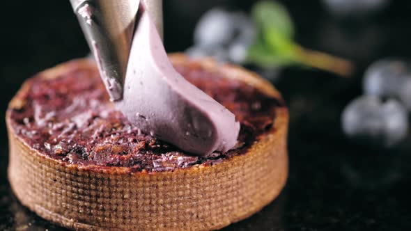 Pastry Chef Decorates Biscuit with Purple Cream From Pastry Bag, Close-up.