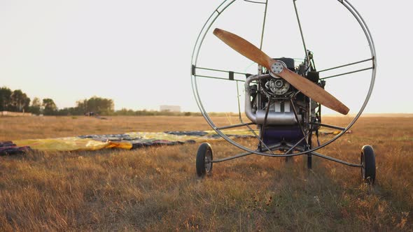 The Motor Paraglider Stands in the Field at Sunset with a Wooden Propeller, and the Pilot Lays Out