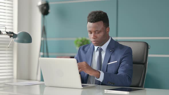 African Businessman Looking at Camera While Using Laptop in Office