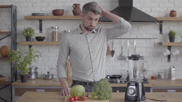 Handsome Thoughtful Good-looking Man in the Shirt Standing at the Table with a Blender