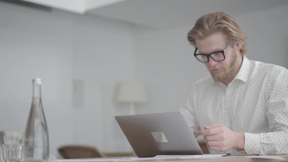 Portrait Thoughtful Businessman in Glasses Sitting at the Table in a Light Comfortable Office