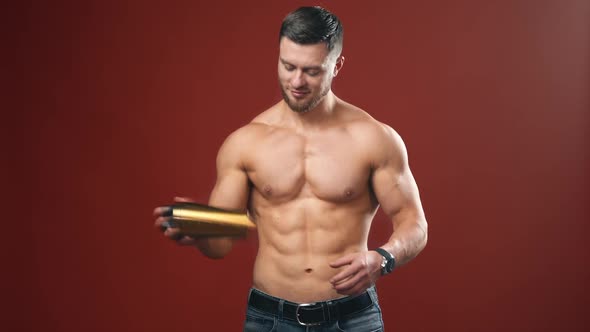 Very muscular sporty guy drinking protein in dark red background with naked torso. Athletic body.
