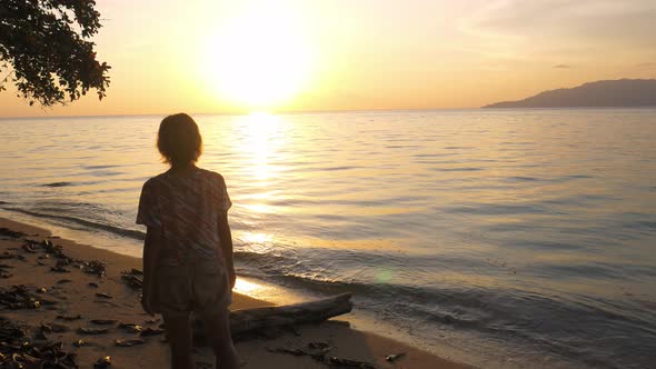 Woman relaxing on sand beach romantic sky at sunset, rear view, golden clouds