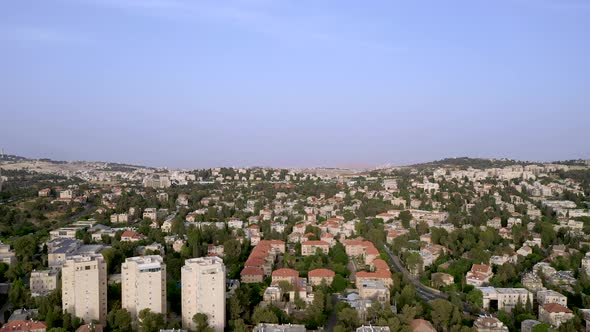 Aerial Forward fly over Jerusalem red roof neighborhood filled with trees at clear day, drone shot,