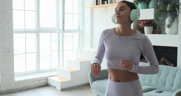 Young Trendy Woman in Big Headphones Listening Music and Dancing at Home