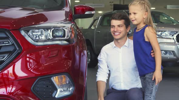 A Young Father and Daughter Are Standing Near One of the Cars