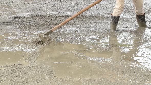 Worker using hoe to smooth wet cement surface