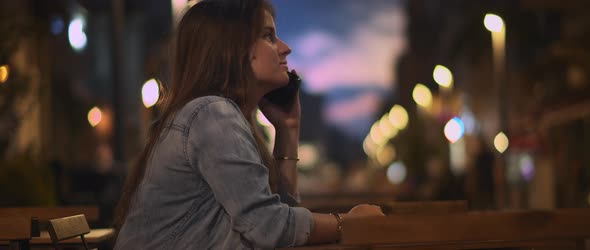 A young woman in denim shirt talking on the phone in a city cafe