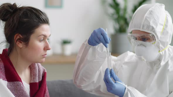 Female Doctor in Protective Suit Collecting Nasal Swab from Woman at Home