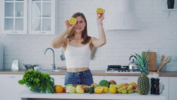 Young woman with oranges in the kitchen and many fresh fruit and vegetables on the table