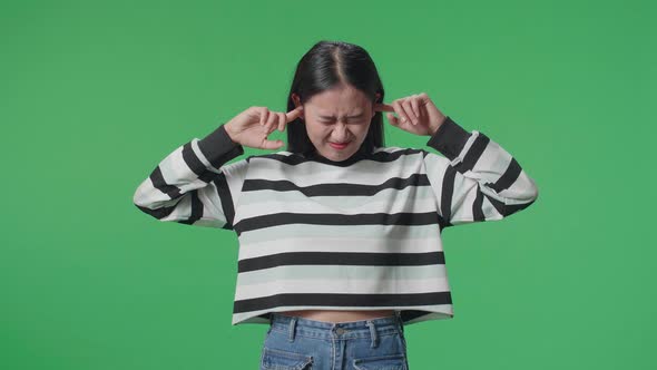 Stressed Asian Woman Covering Her Ears While Standing In Front Of Green Screen Background