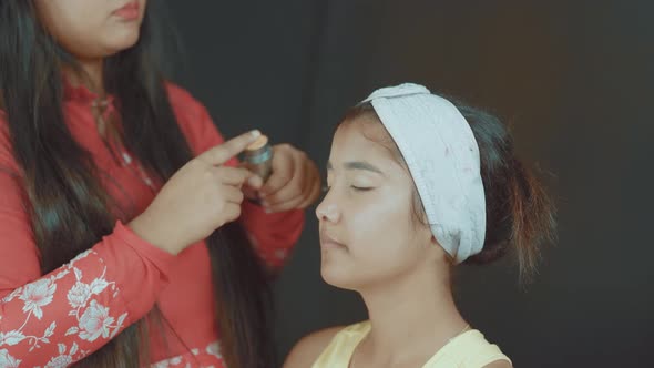 Close up of professional make up artist putting a face powder on woman's face and make up her