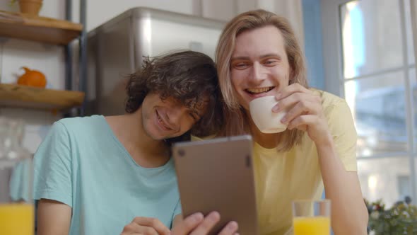 Male Gay Couple Looking at Tablet Computer Over Breakfast