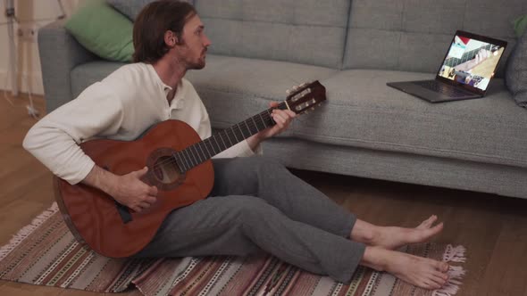 Concentrated long-haired man learns to play the guitar from a video lesson