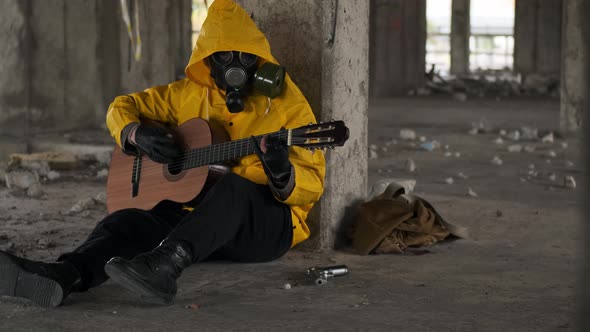 Unrecognizable Man or Woman in Yellow Protective Suit and Gas Mask Sits on Floor in Abandoned