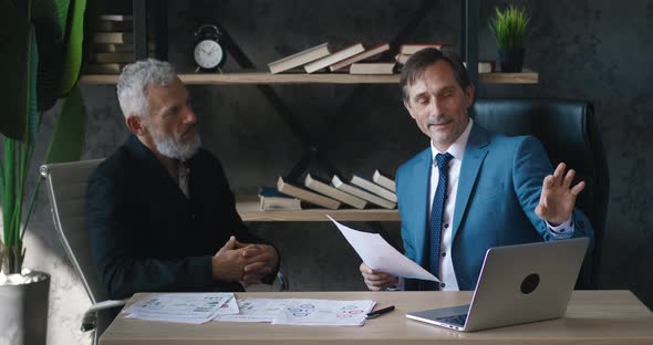 Two Businessmen Using a Laptop and Having a Discussion in a Modern Office