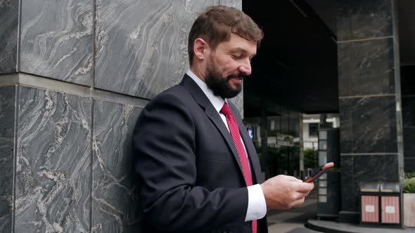 A Serious Middleaged Businessman in Luxurious Clothes in the Financial District of a Metropolis Uses